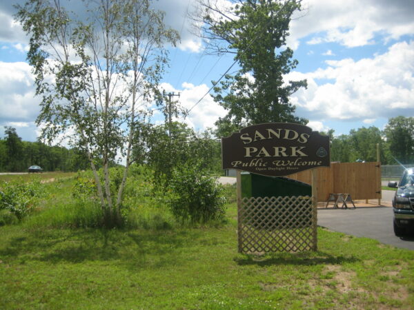 Sands Park entrance sign with trees and sky.